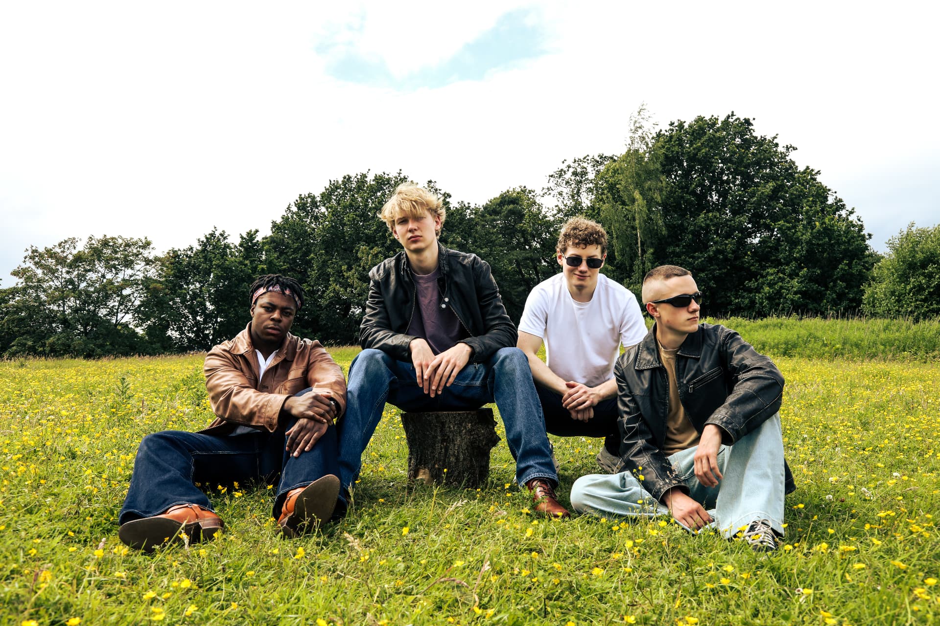 SOMNIAC band press photo, four members sitting in a buttercup field with trees behind them