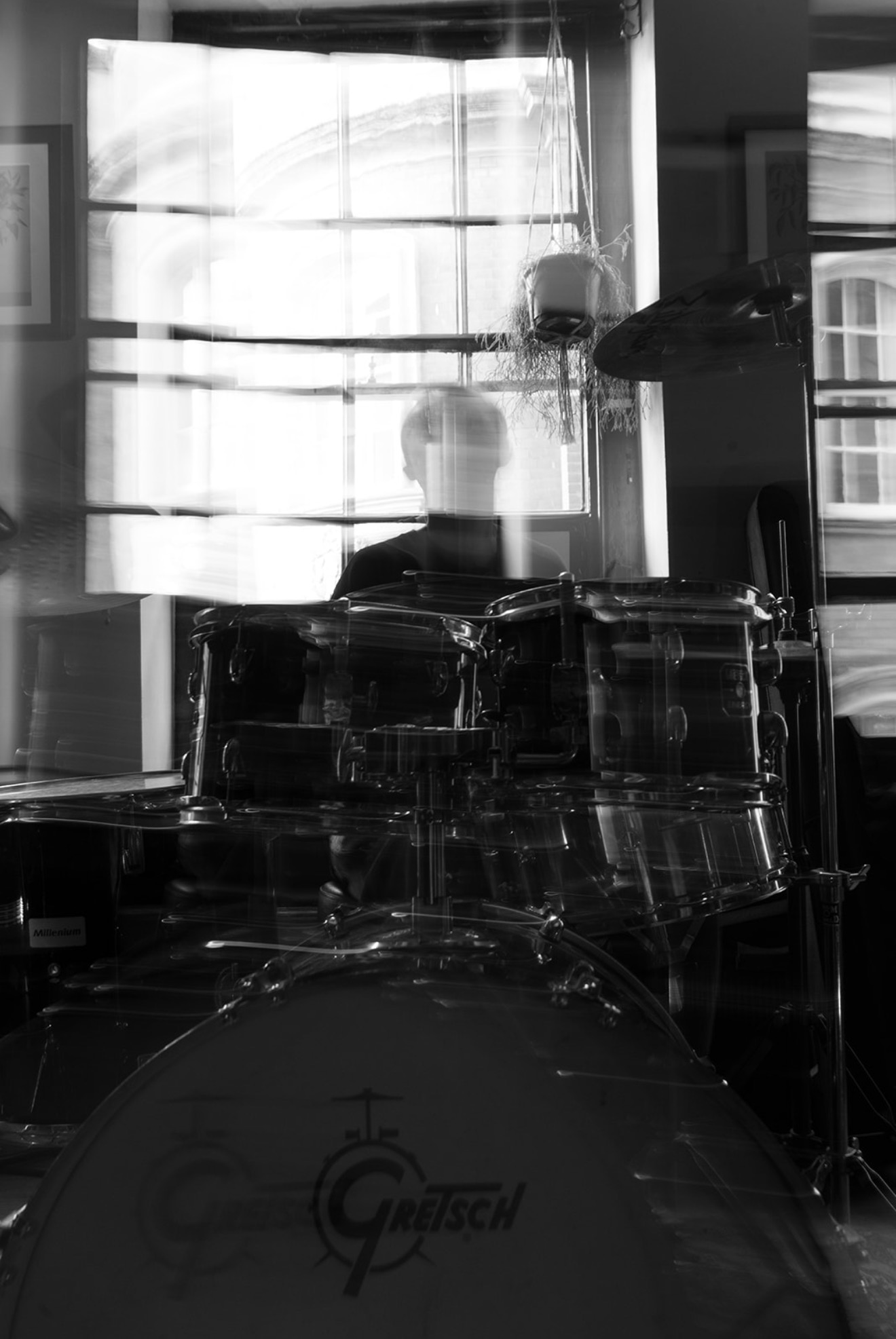Black and white photo of a drummer and Gretsch drum kit in a rehearsal room, motion blur through the window light