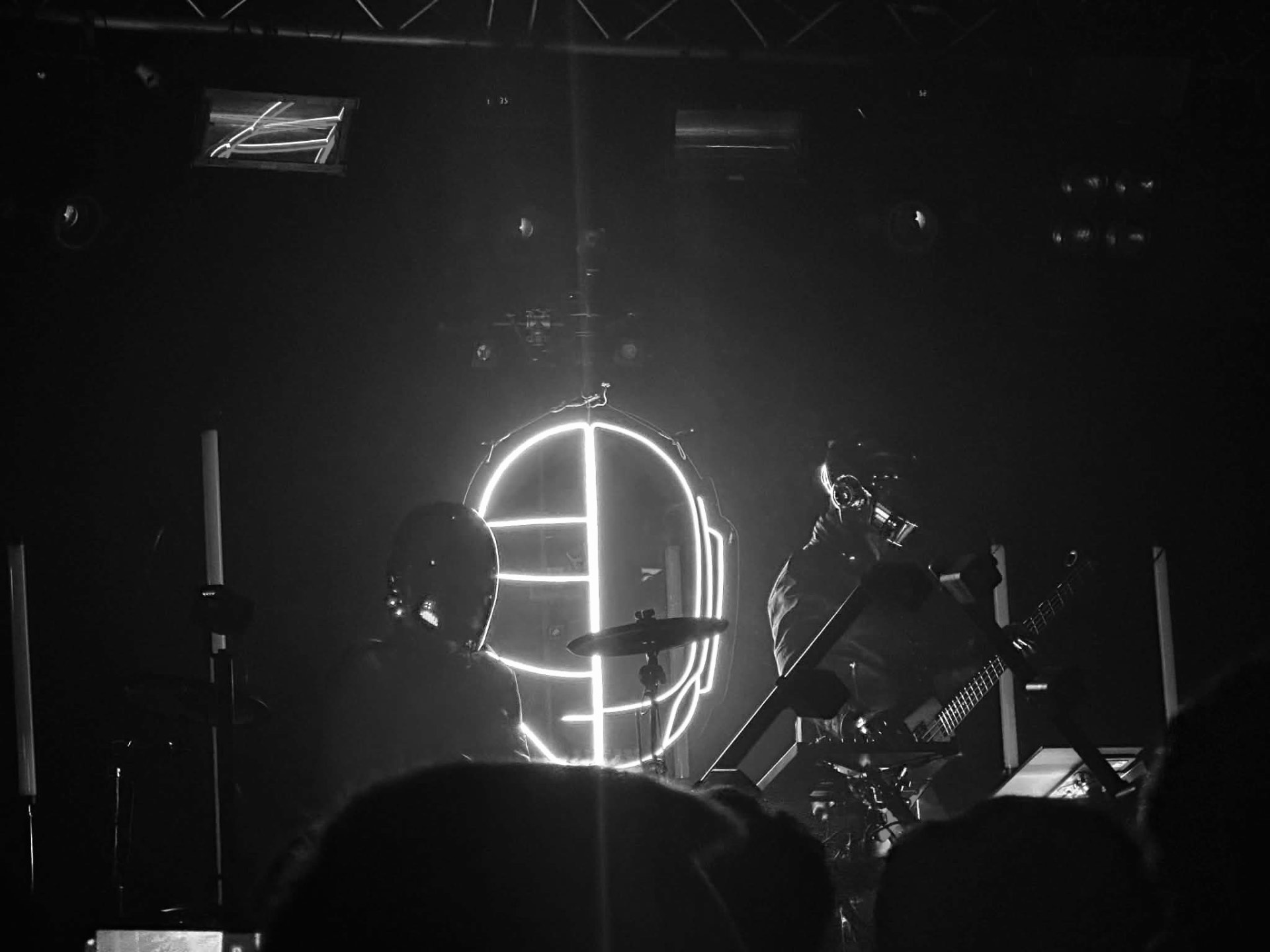 Band on a dark club stage with a large glowing neon helmet backdrop