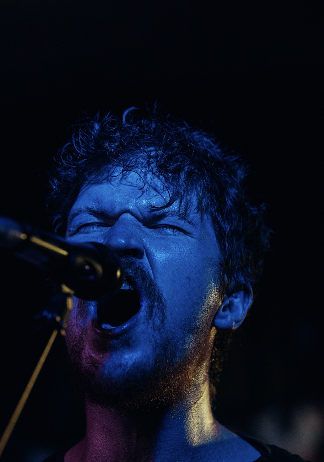 Vocalist screaming into a microphone, face bathed in deep blue stage light against blackness