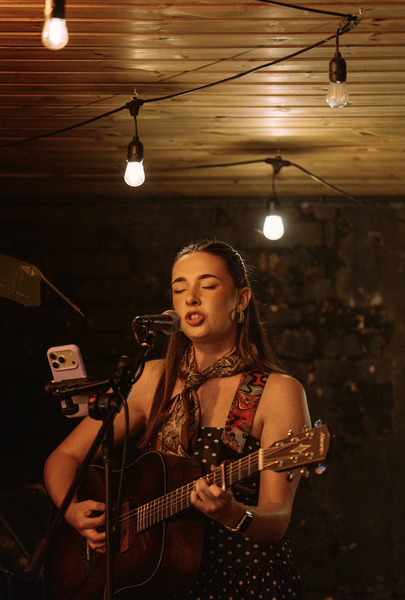 Singer-songwriter with an acoustic guitar performing under warm string lights